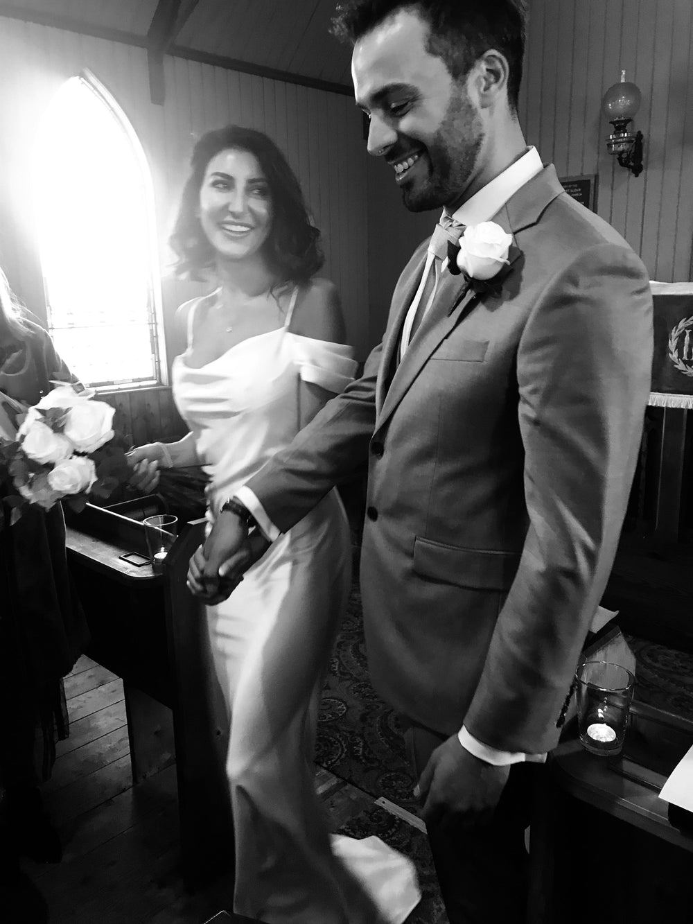 Black and white photo of a couple on their wedding day, smiling and holding hands.