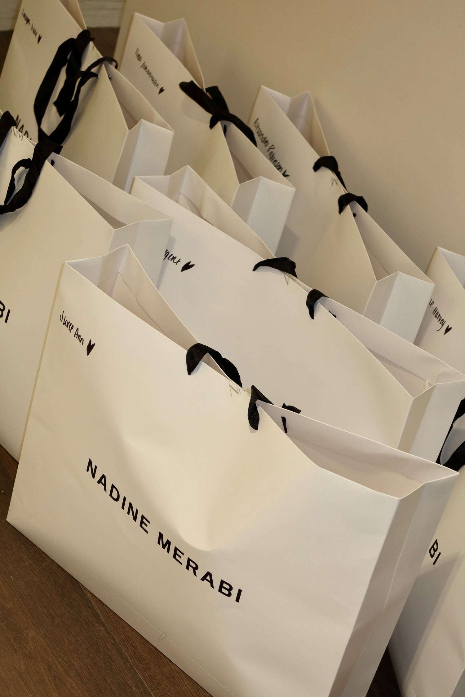 White shopping bags with 'Nadine Merabi' branding on a wooden surface.