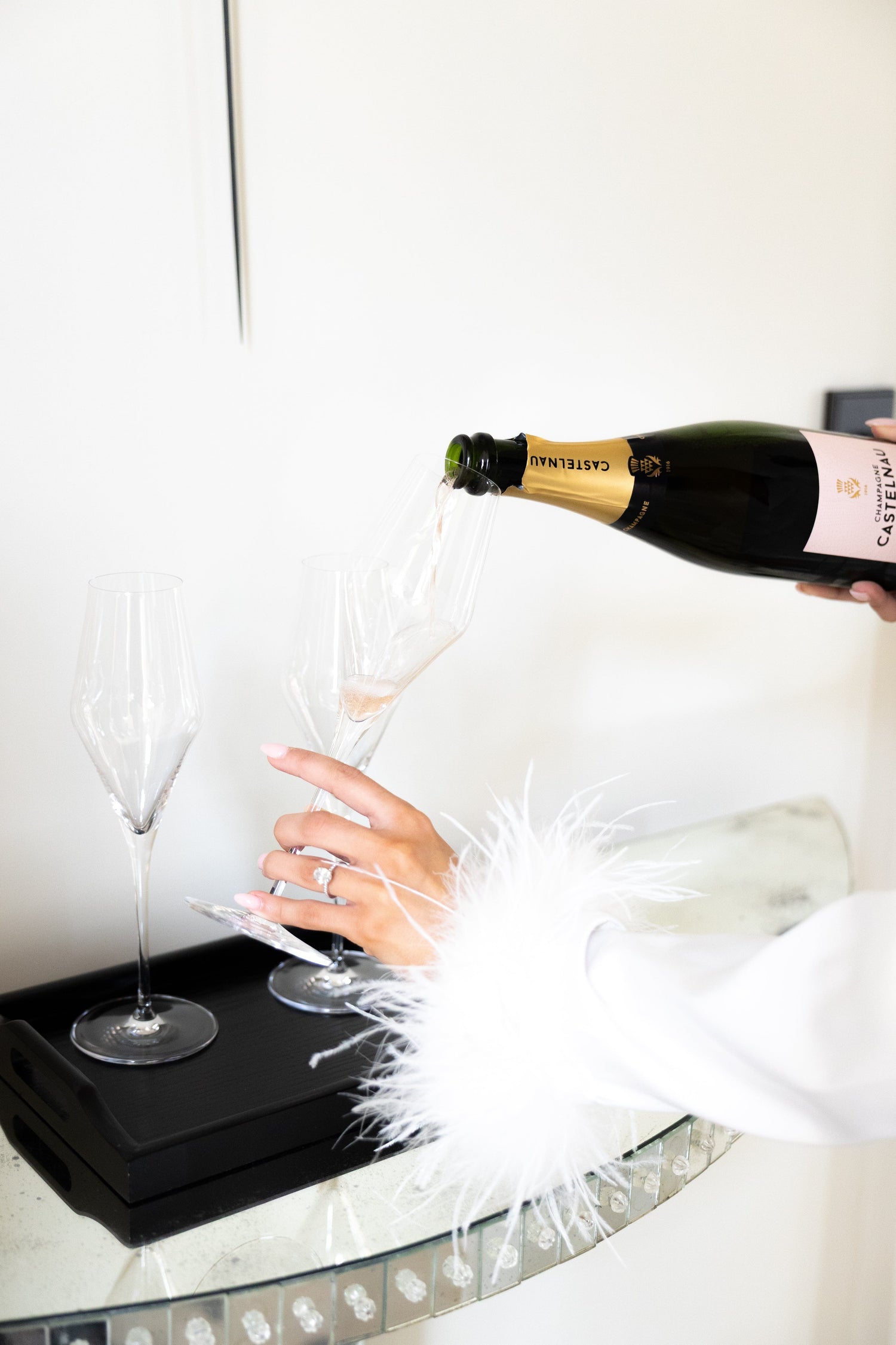 Person pouring champagne from a bottle into a glass on a white surface.