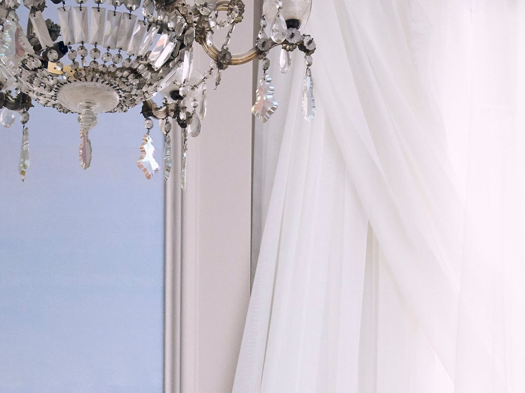 Chandelier with crystal accents hanging above a white curtain.