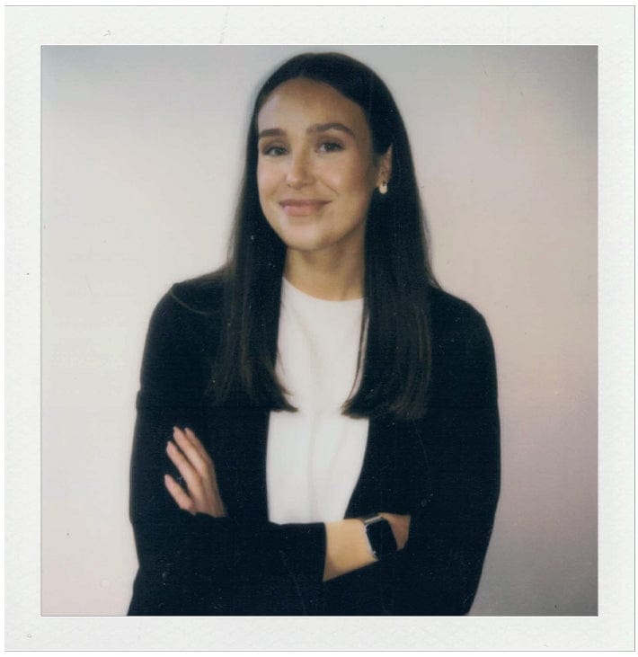 Woman with arms crossed wearing a black blazer over a white shirt on a plain background