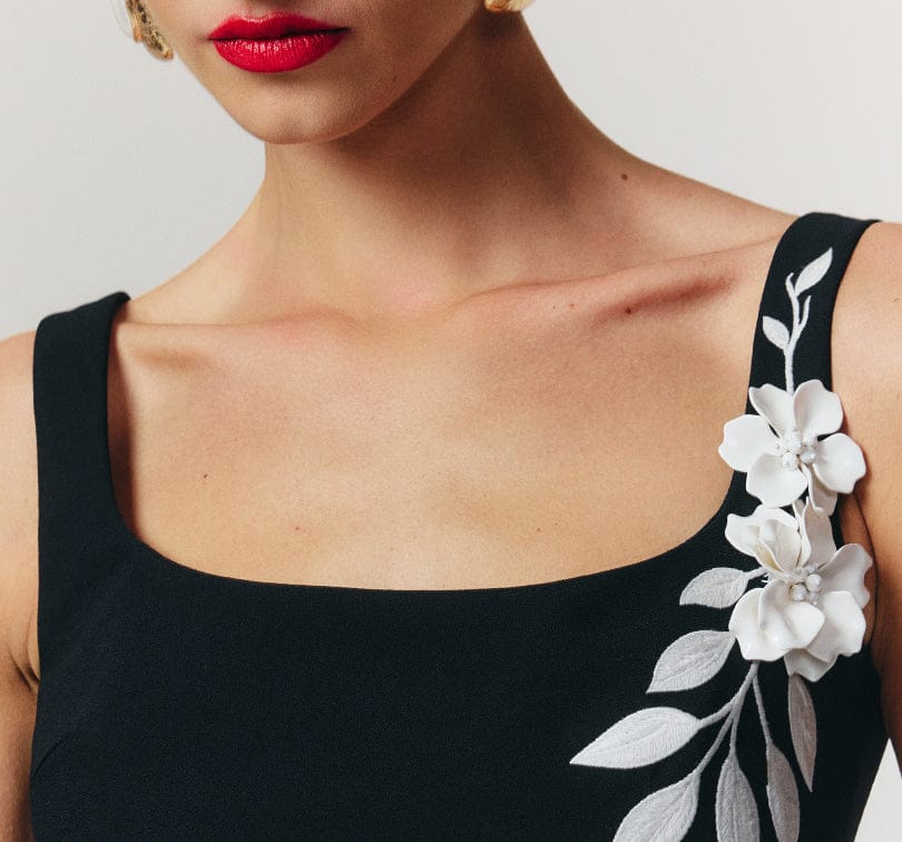 Black sleeveless top with white floral embroidery on a plain background