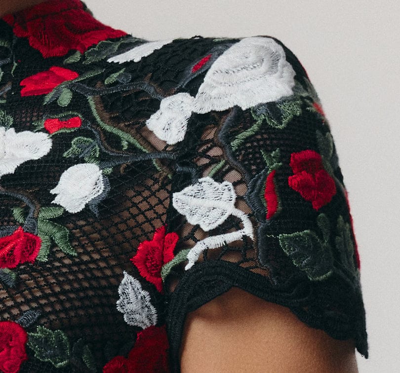 Close-up of a black lace top with red and white floral embroidery on a neutral background