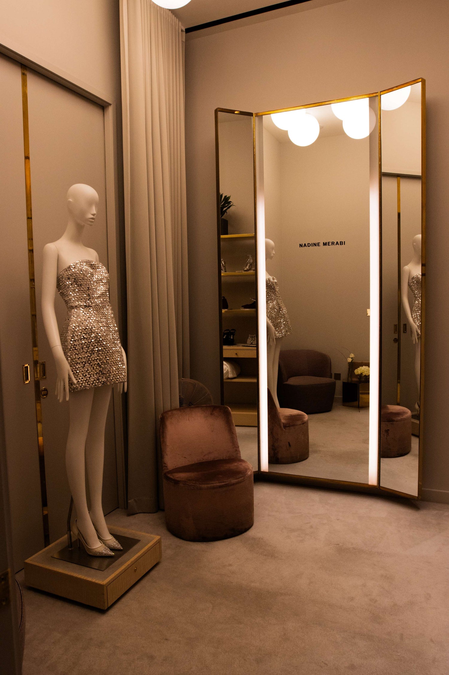 Mannequin wearing a sparkling dress in front of a large mirror in an interior setting.