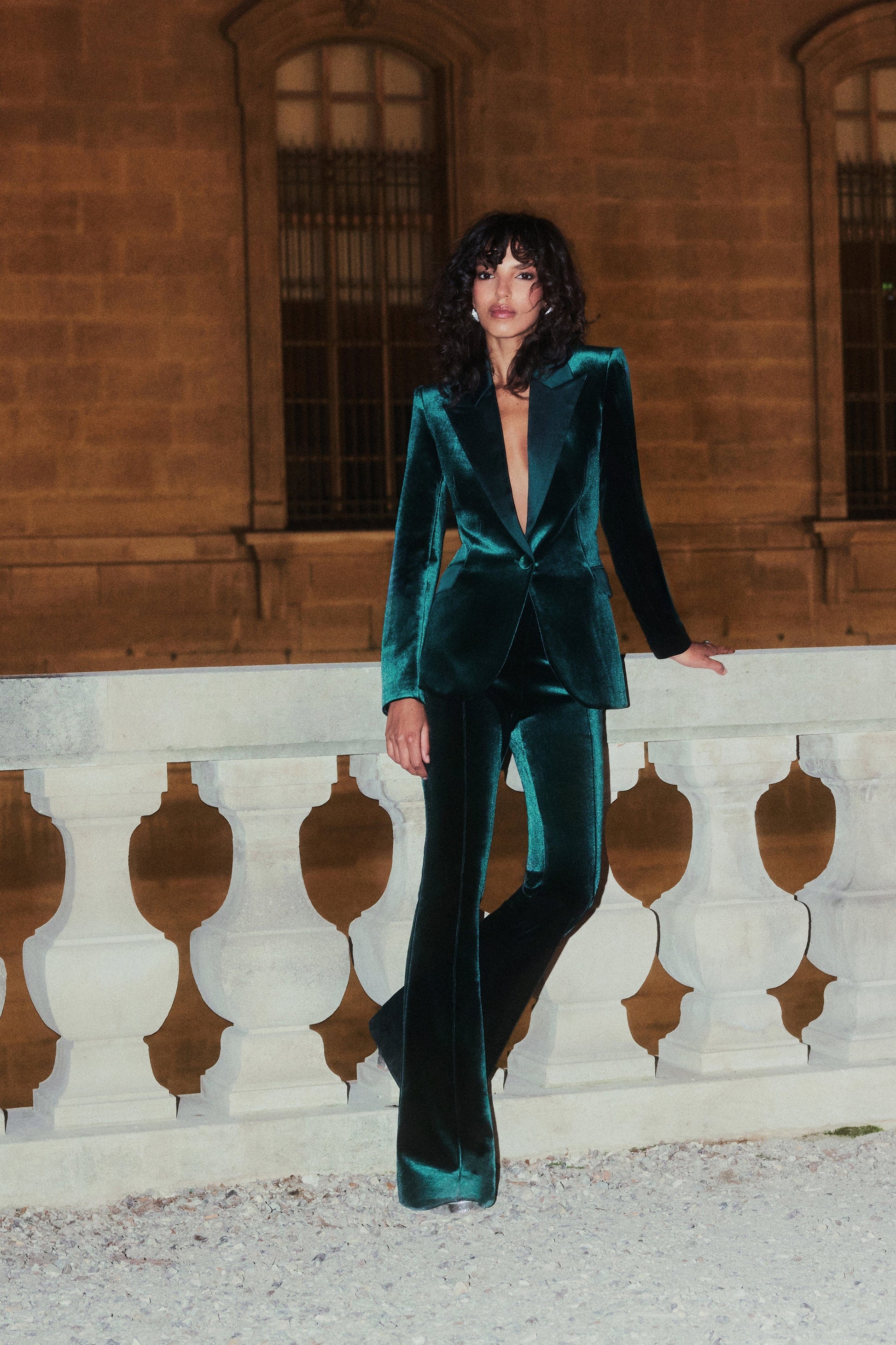 Woman in a teal velvet suit standing against a stone wall.