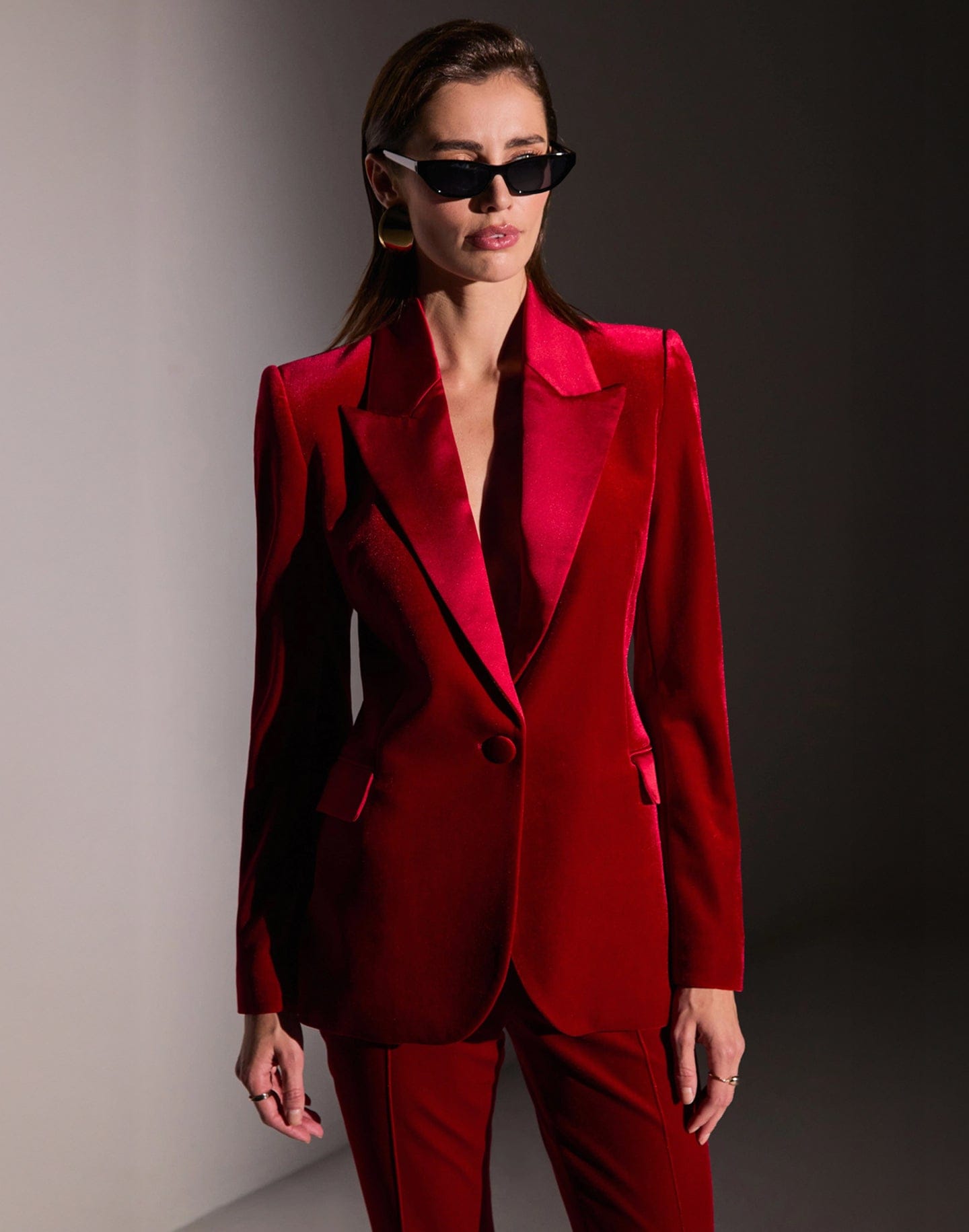 Woman wearing a red suit and sunglasses against a neutral background