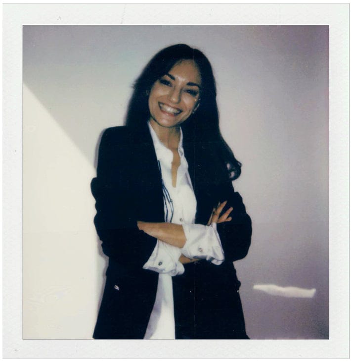 Person wearing a black blazer over a white shirt against a plain background
