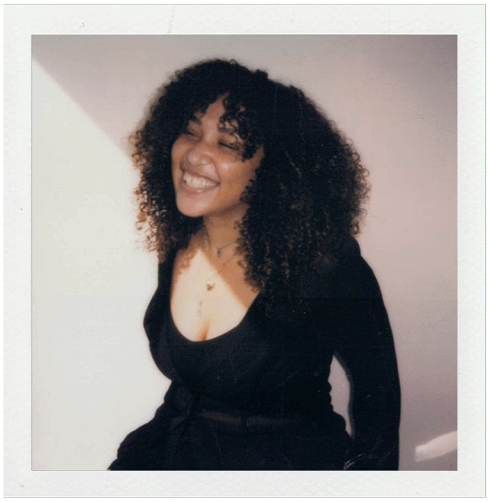 Woman with curly hair wearing a black top against a plain background